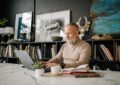 An elderly man focused on his laptop in a beautifully decorated home office setting.