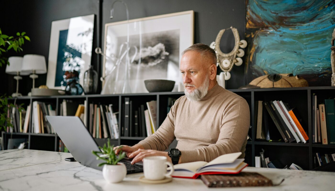 An elderly man focused on his laptop in a beautifully decorated home office setting.